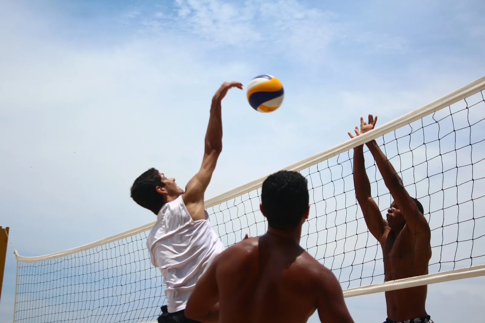 Friends playing beach volleyball, mid-spike