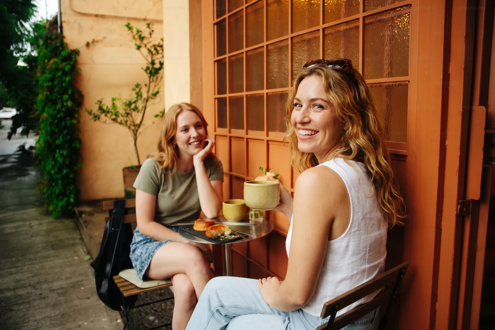 Two friends smiling at a café table outside