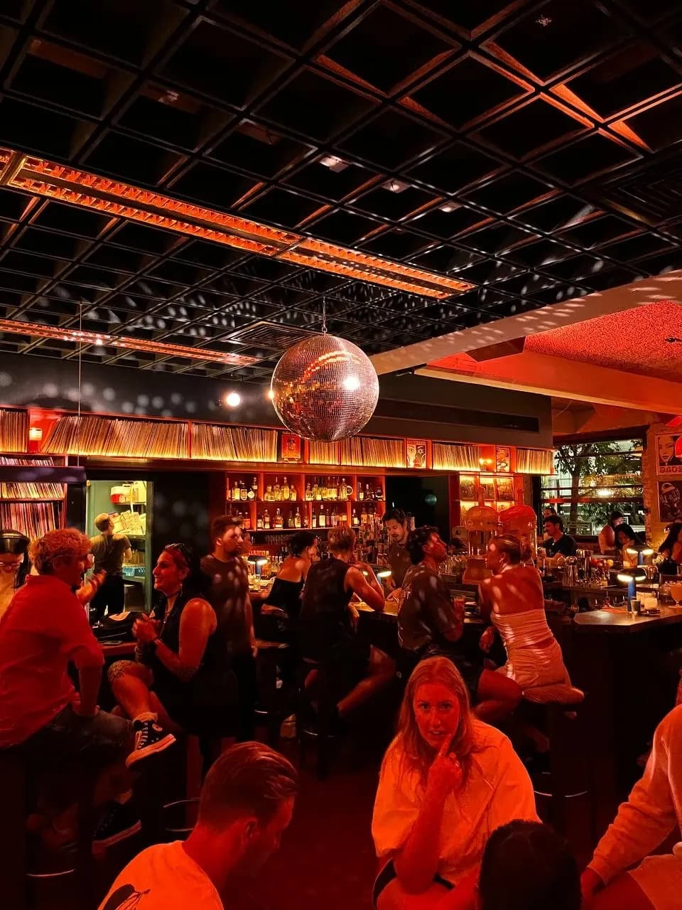 A busy bar lit red, with a disco ball and friends talking