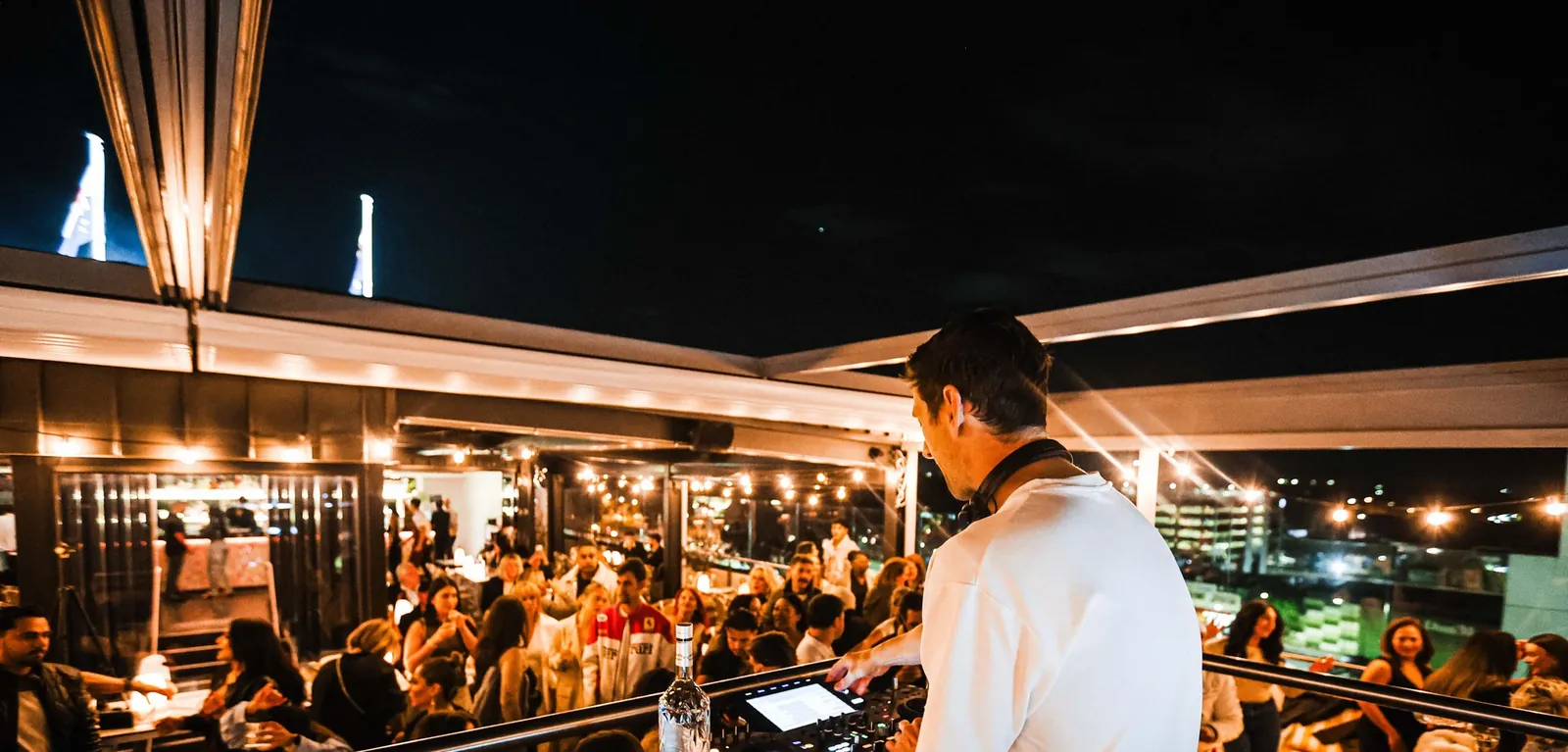 A rooftop bar at night with a DJ and a crowd
